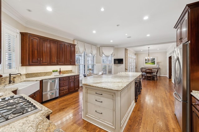 kitchen featuring appliances with stainless steel finishes, a center island, ornamental molding, pendant lighting, and light hardwood / wood-style flooring