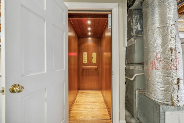 interior space featuring elevator, hardwood / wood-style floors, wooden walls, and heating unit