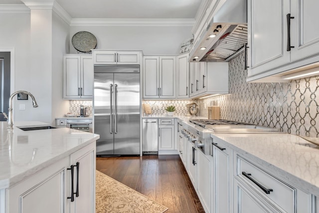 kitchen featuring appliances with stainless steel finishes, crown molding, light stone counters, and range hood