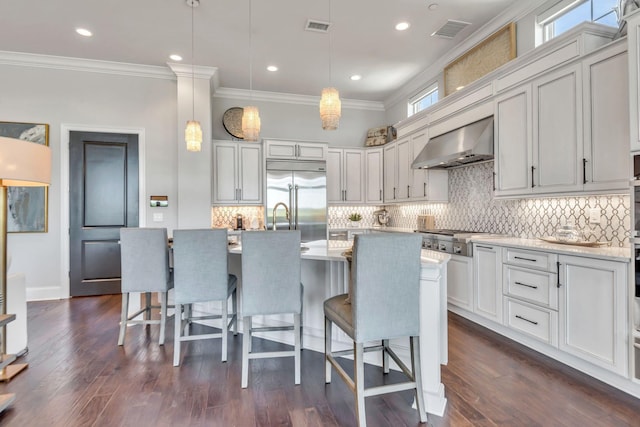 kitchen featuring appliances with stainless steel finishes, decorative light fixtures, a kitchen island with sink, and range hood