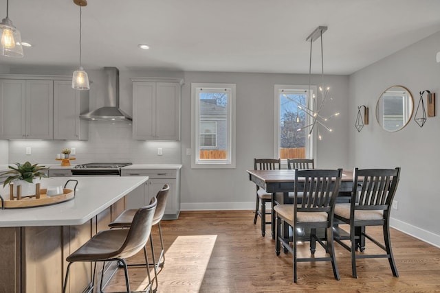 kitchen with wall chimney range hood, decorative light fixtures, tasteful backsplash, and gray cabinets