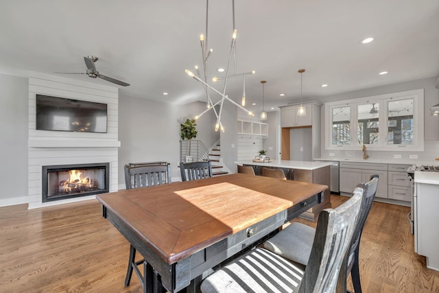 dining space with a fireplace, sink, light hardwood / wood-style flooring, and ceiling fan