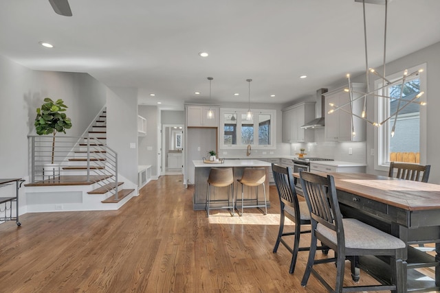 kitchen featuring hanging light fixtures, wall chimney range hood, a kitchen island, light wood-type flooring, and backsplash