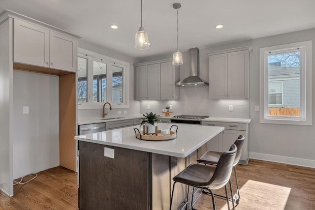 kitchen featuring hardwood / wood-style flooring, wall chimney range hood, a kitchen island, sink, and pendant lighting