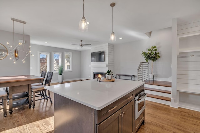 kitchen featuring decorative light fixtures, oven, a fireplace, ceiling fan with notable chandelier, and light hardwood / wood-style floors