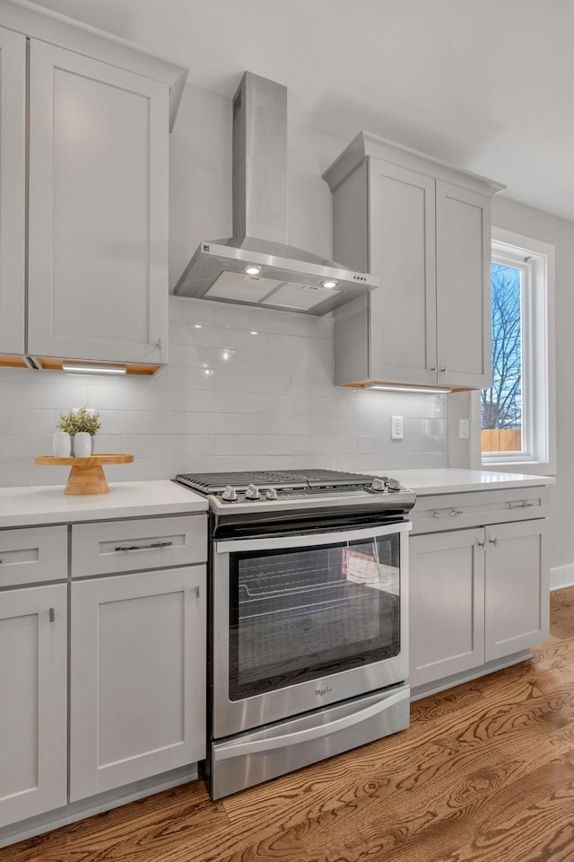 kitchen featuring light hardwood / wood-style flooring, decorative backsplash, stainless steel gas range, and wall chimney range hood