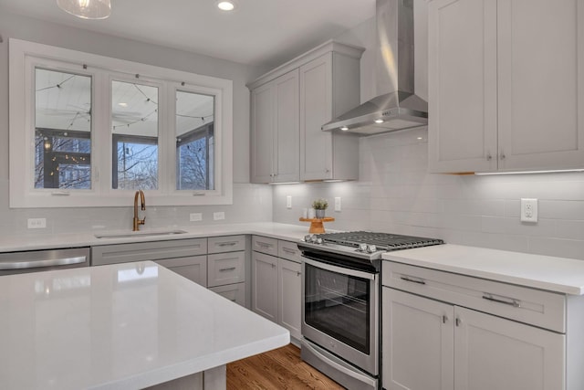 kitchen with sink, wall chimney range hood, light hardwood / wood-style floors, decorative backsplash, and stainless steel appliances