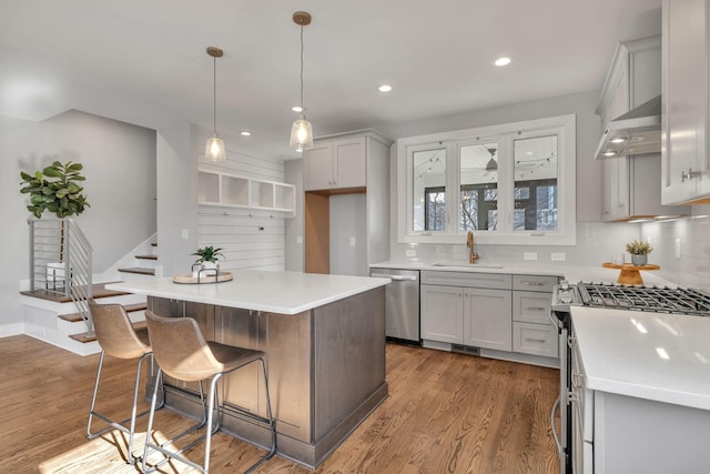 kitchen featuring a center island, hardwood / wood-style floors, appliances with stainless steel finishes, hanging light fixtures, and wall chimney range hood