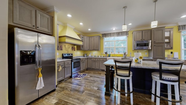 kitchen featuring a breakfast bar area, appliances with stainless steel finishes, premium range hood, light stone counters, and decorative light fixtures