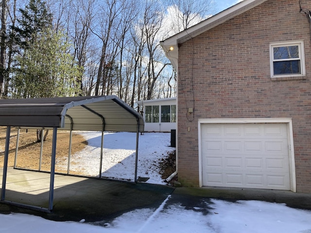 view of snow covered exterior featuring a garage, a carport, and a sunroom