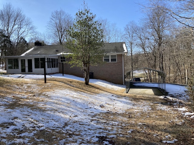 snow covered rear of property featuring a carport and a sunroom