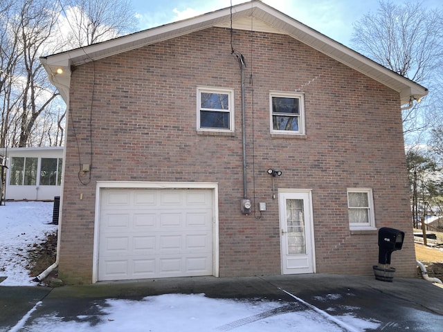 snow covered rear of property featuring a sunroom and a garage