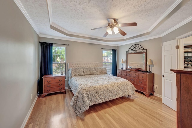 bedroom featuring light hardwood / wood-style floors, ceiling fan, ornamental molding, a tray ceiling, and a textured ceiling