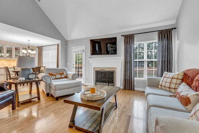 living room with lofted ceiling, a chandelier, light hardwood / wood-style flooring, and a healthy amount of sunlight