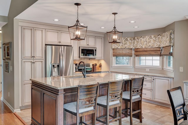 kitchen featuring decorative light fixtures, light stone counters, a kitchen island with sink, a notable chandelier, and appliances with stainless steel finishes