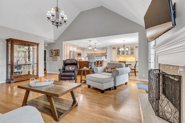 living room featuring a premium fireplace, high vaulted ceiling, a notable chandelier, and light hardwood / wood-style flooring