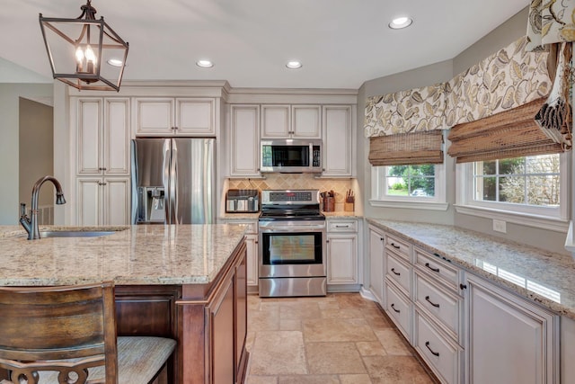 kitchen featuring appliances with stainless steel finishes, light stone countertops, a kitchen island, sink, and decorative light fixtures