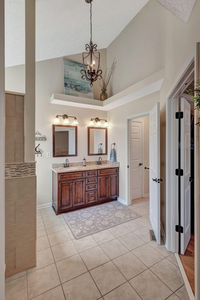 bathroom with high vaulted ceiling, an inviting chandelier, tile patterned floors, and vanity