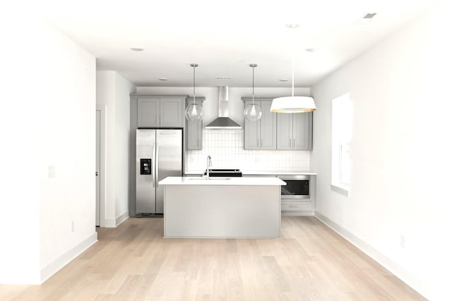 kitchen with gray cabinets, a center island with sink, decorative backsplash, stainless steel refrigerator with ice dispenser, and wall chimney range hood