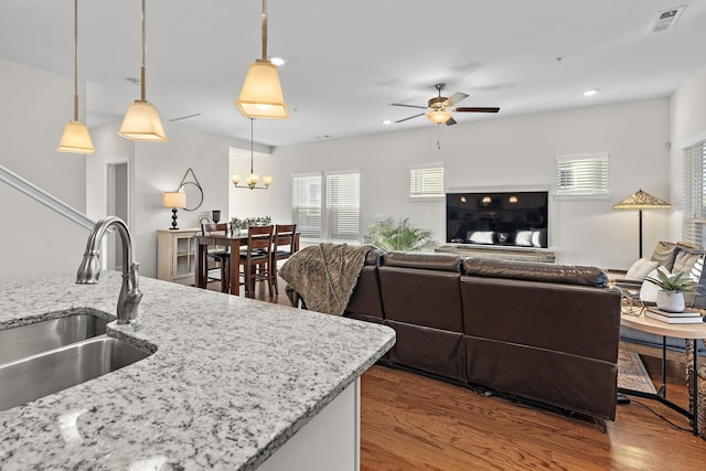 kitchen featuring light stone countertops, hanging light fixtures, ceiling fan with notable chandelier, wood-type flooring, and sink