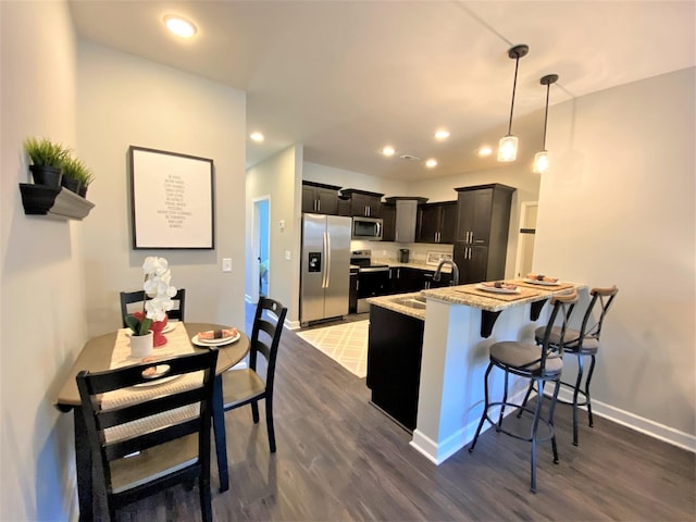 kitchen with a kitchen breakfast bar, appliances with stainless steel finishes, dark wood-type flooring, sink, and decorative light fixtures