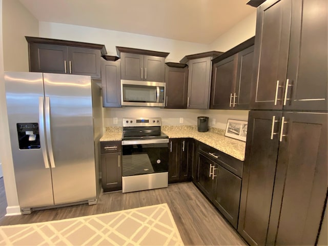 kitchen with hardwood / wood-style flooring, appliances with stainless steel finishes, light stone countertops, and dark brown cabinetry