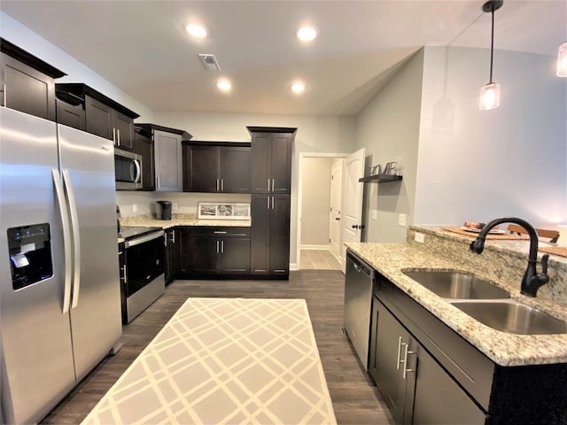 kitchen with sink, appliances with stainless steel finishes, light stone countertops, pendant lighting, and dark wood-type flooring