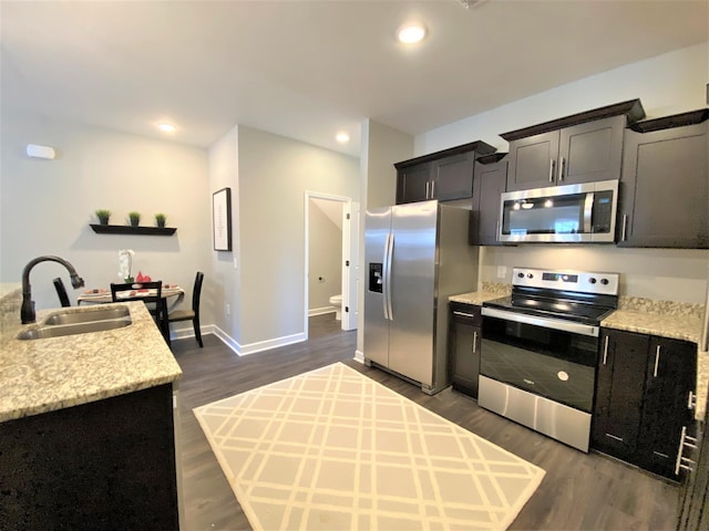 kitchen featuring light stone counters, dark hardwood / wood-style floors, stainless steel appliances, a kitchen island with sink, and sink