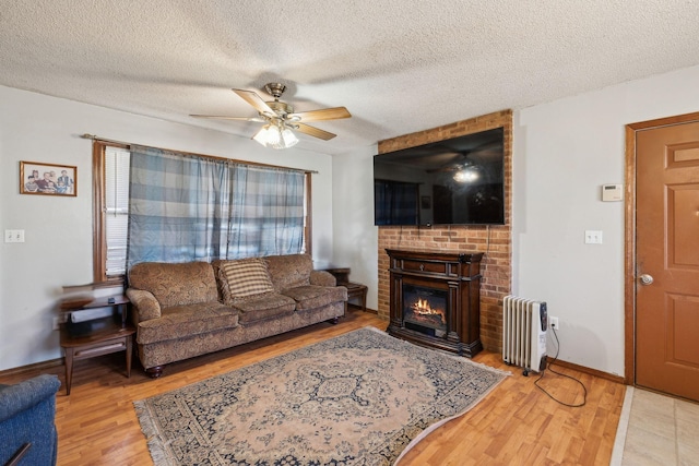 living room with a brick fireplace, radiator, hardwood / wood-style floors, and a textured ceiling