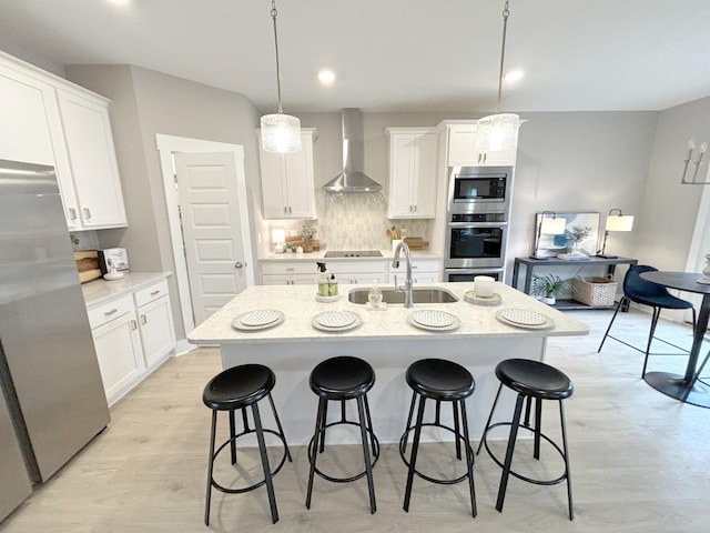 kitchen featuring stainless steel appliances, pendant lighting, wall chimney exhaust hood, sink, and white cabinetry