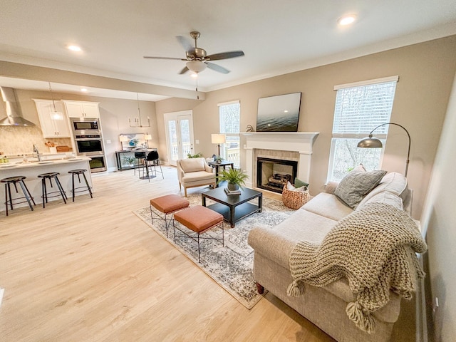 living room with ceiling fan, light hardwood / wood-style flooring, crown molding, and a fireplace