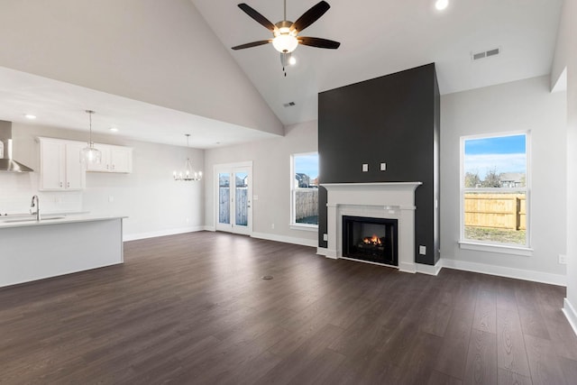 unfurnished living room featuring sink, dark hardwood / wood-style flooring, high vaulted ceiling, and ceiling fan with notable chandelier