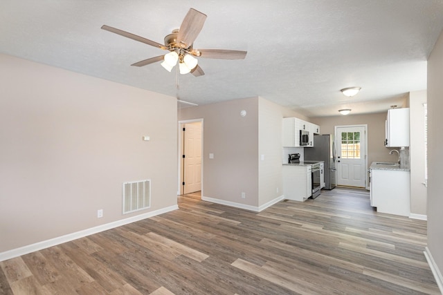 unfurnished living room featuring a textured ceiling, ceiling fan, wood-type flooring, and sink