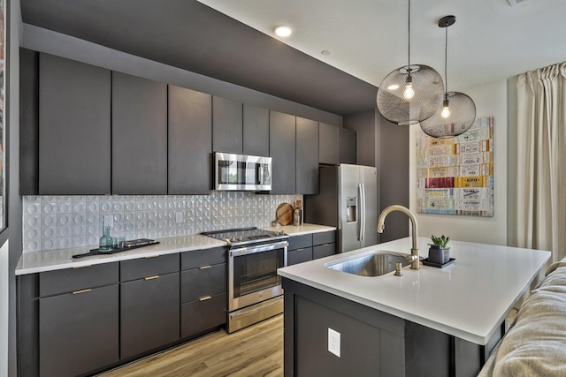 kitchen featuring stainless steel appliances, sink, decorative light fixtures, backsplash, and a kitchen island with sink