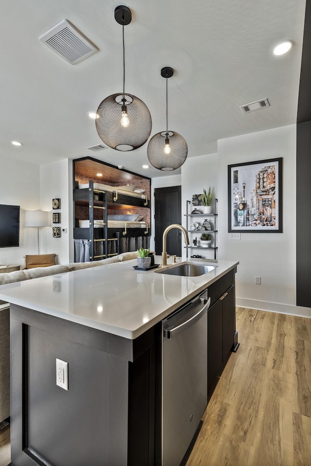 kitchen featuring sink, dishwasher, light wood-type flooring, an island with sink, and hanging light fixtures