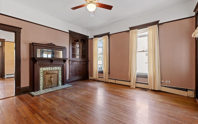 unfurnished living room with wood-type flooring, a tile fireplace, baseboard heating, and ceiling fan