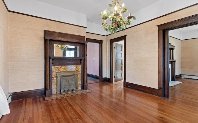 unfurnished living room with a baseboard heating unit, an inviting chandelier, hardwood / wood-style flooring, and a fireplace