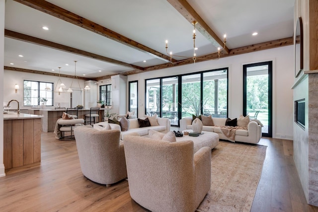 living room featuring sink, an inviting chandelier, light hardwood / wood-style floors, and beamed ceiling