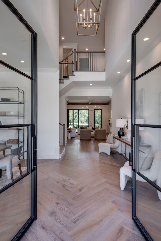 foyer featuring an inviting chandelier, a towering ceiling, and light parquet flooring