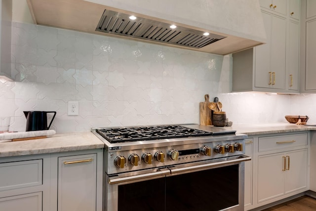 kitchen featuring light stone counters, wall chimney range hood, backsplash, and double oven range