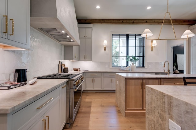 kitchen featuring custom range hood, high end stove, white cabinetry, decorative light fixtures, and tasteful backsplash