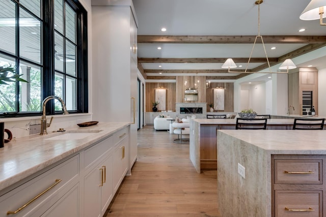 kitchen with pendant lighting, a large island, beam ceiling, white cabinets, and sink