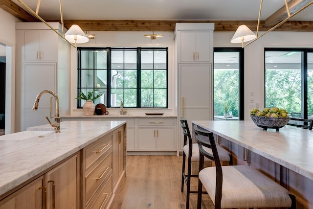 kitchen with light stone counters, decorative light fixtures, light wood-type flooring, white cabinetry, and sink