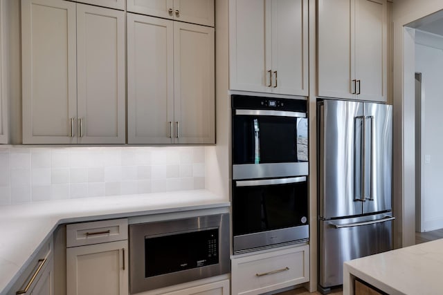 kitchen featuring light stone countertops, stainless steel appliances, gray cabinetry, and tasteful backsplash