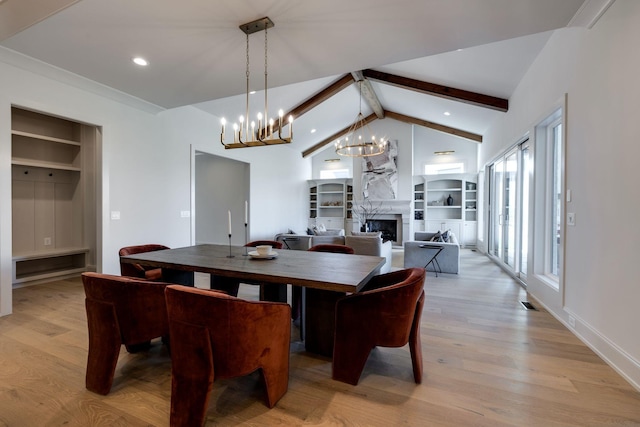 dining space featuring a high end fireplace, lofted ceiling with beams, a chandelier, and light hardwood / wood-style flooring