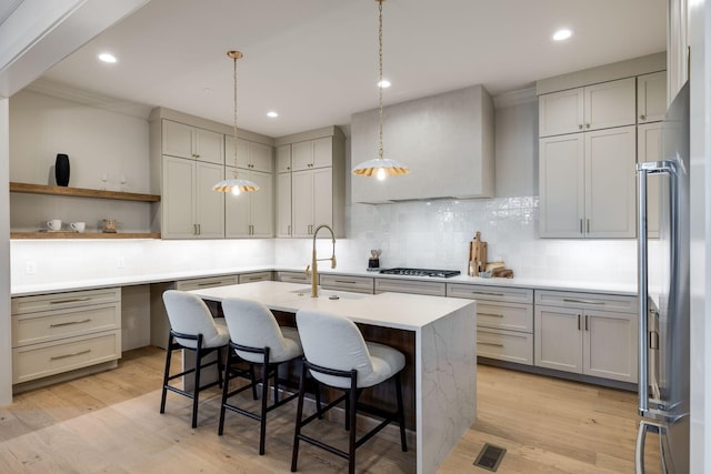 kitchen with stainless steel appliances, an island with sink, a kitchen bar, decorative backsplash, and light hardwood / wood-style flooring