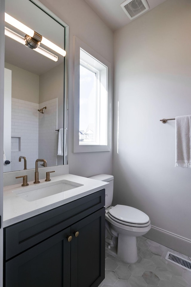 bathroom featuring vanity, a tile shower, tile patterned floors, and toilet