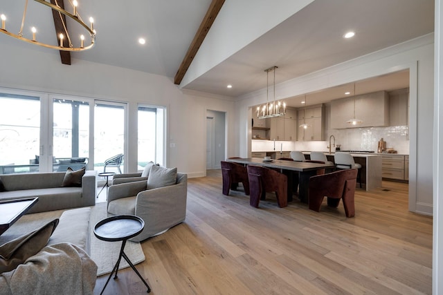 living room featuring light wood-type flooring, lofted ceiling with beams, a chandelier, and sink