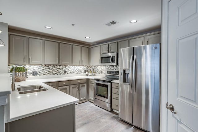 kitchen with light hardwood / wood-style floors, stainless steel appliances, gray cabinetry, decorative backsplash, and sink