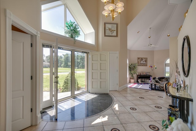 foyer entrance with a high ceiling, ceiling fan with notable chandelier, and light tile patterned floors